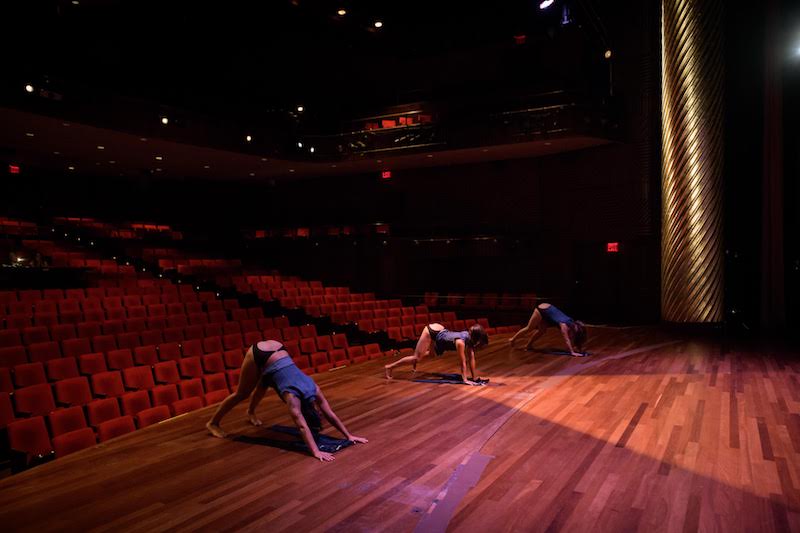 Three women crouch with their hands and feet on the ground while their haunches face out to the auditorium. 
